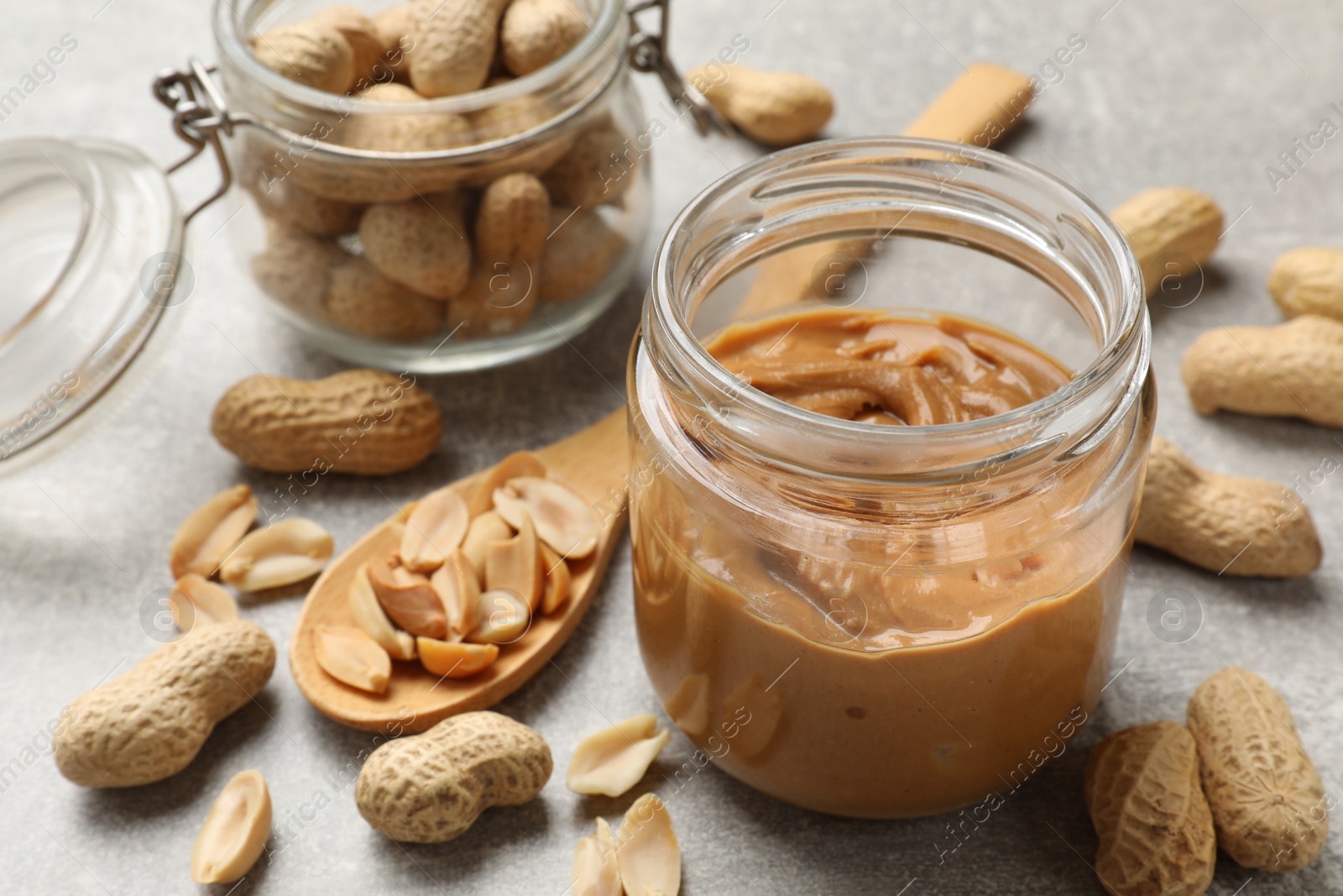 Photo of Tasty peanut butter in jar and groundnuts on grey textured table