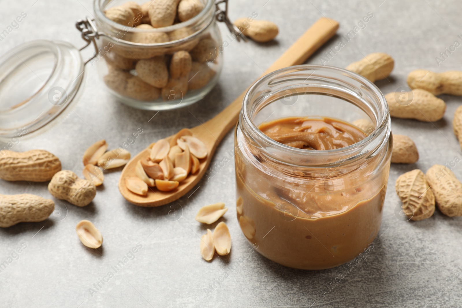 Photo of Tasty peanut butter in jar and groundnuts on grey textured table