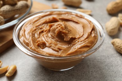 Photo of Tasty peanut butter in glass bowl on grey textured table, closeup