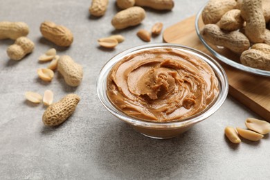 Photo of Tasty peanut butter in bowl and groundnuts on grey textured table