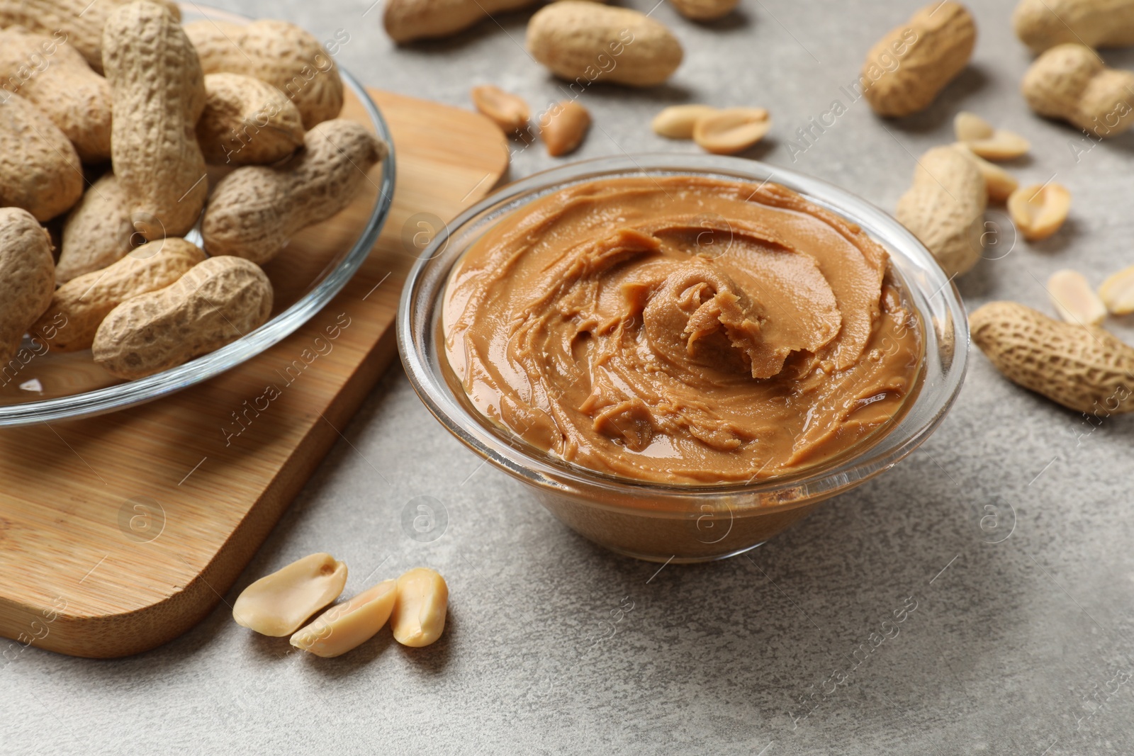 Photo of Tasty peanut butter in bowl and groundnuts on grey textured table