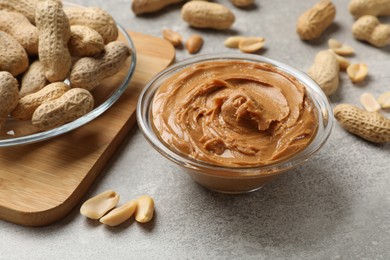 Tasty peanut butter in bowl and groundnuts on grey textured table