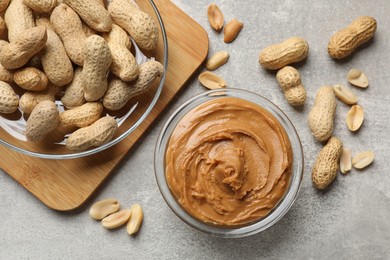 Photo of Tasty peanut butter in bowl and groundnuts on grey textured table, flat lay