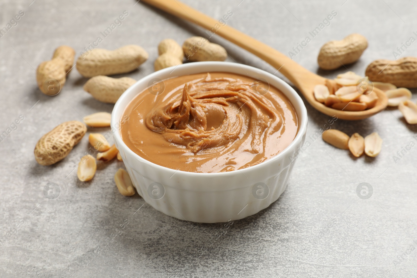 Photo of Tasty peanut butter in bowl and groundnuts on grey textured table