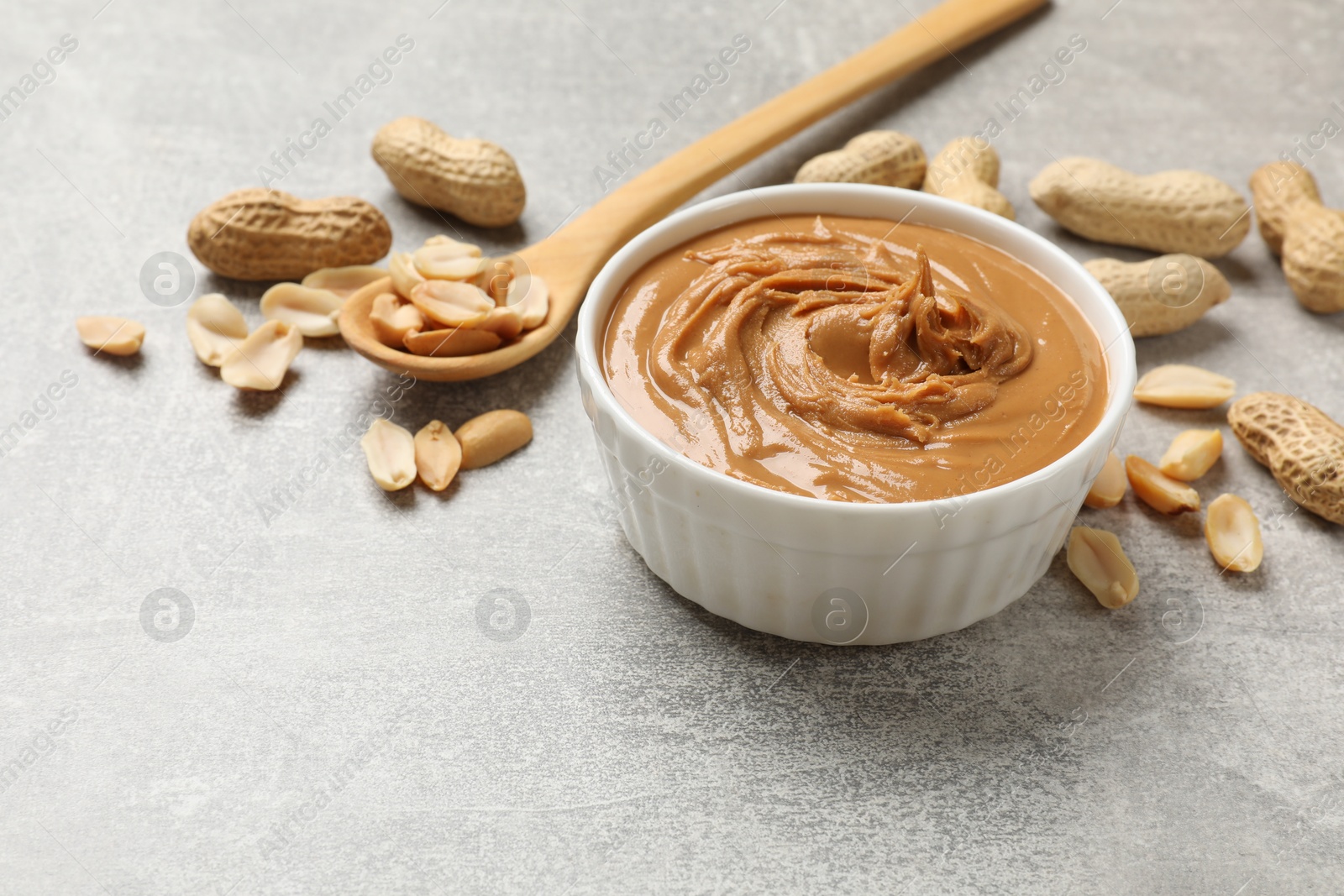 Photo of Tasty peanut butter in bowl and groundnuts on grey textured table