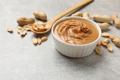 Photo of Tasty peanut butter in bowl and groundnuts on grey textured table