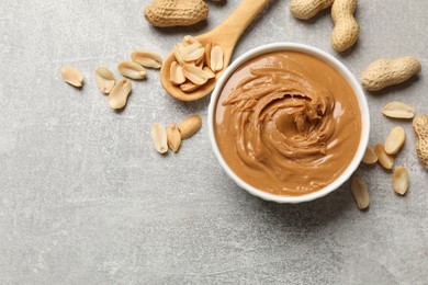 Photo of Tasty peanut butter in bowl and groundnuts on grey textured table, flat lay. Space for text