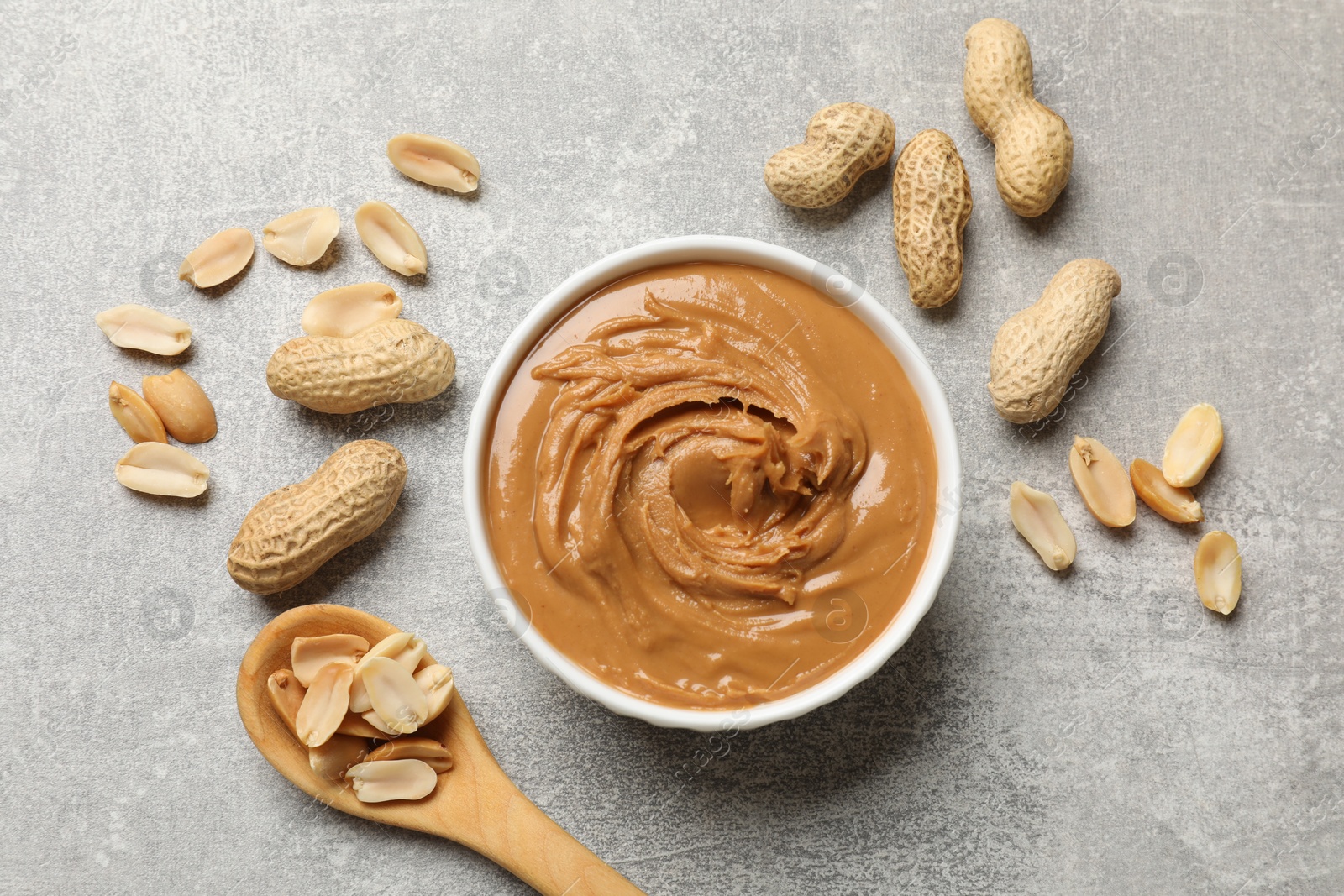 Photo of Tasty peanut butter in bowl and groundnuts on grey textured table, flat lay