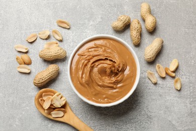 Photo of Tasty peanut butter in bowl and groundnuts on grey textured table, flat lay