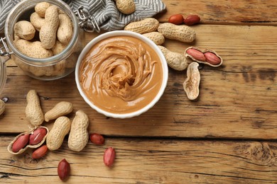 Photo of Tasty peanut butter in bowl and groundnuts on wooden table, flat lay