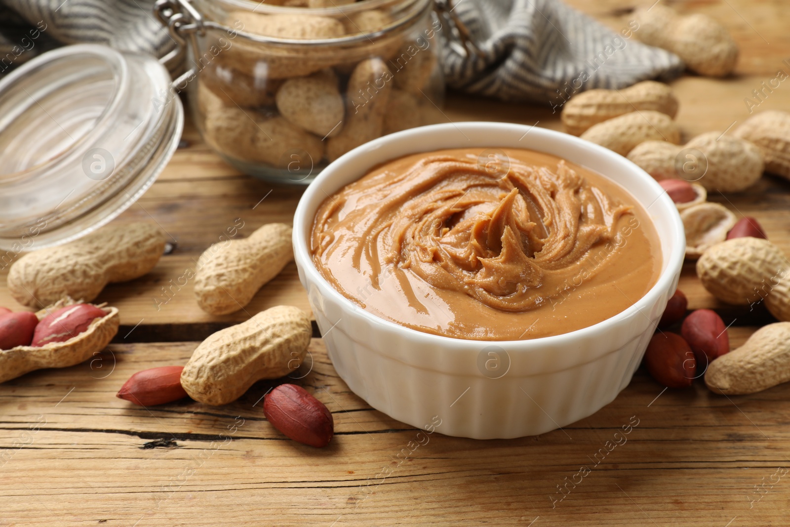 Photo of Tasty peanut butter in bowl and groundnuts on wooden table