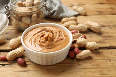 Photo of Tasty peanut butter in bowl and groundnuts on wooden table