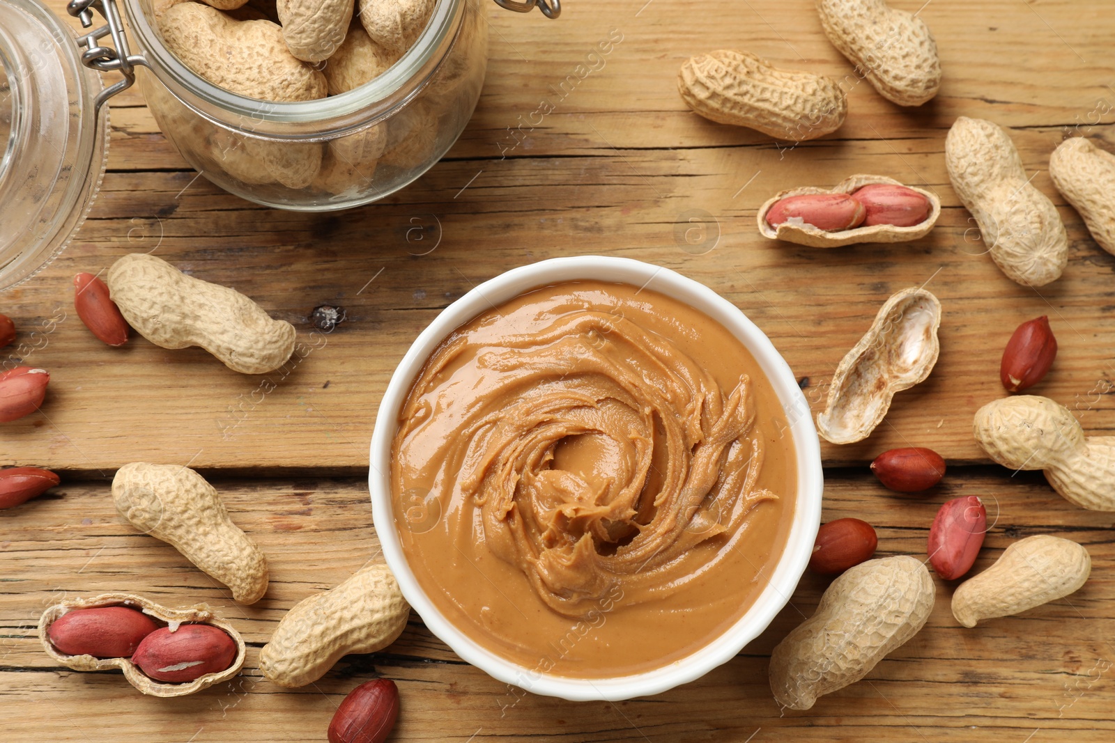 Photo of Tasty peanut butter in bowl and groundnuts on wooden table, flat lay