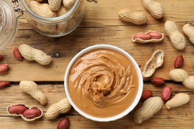 Photo of Tasty peanut butter in bowl and groundnuts on wooden table, flat lay