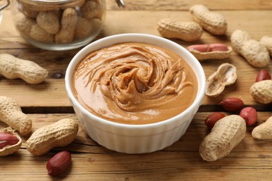 Photo of Tasty peanut butter in bowl and groundnuts on wooden table