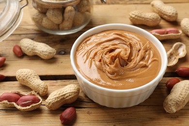 Photo of Tasty peanut butter in bowl and groundnuts on wooden table