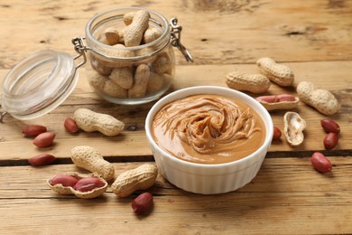 Photo of Tasty peanut butter in bowl and groundnuts on wooden table