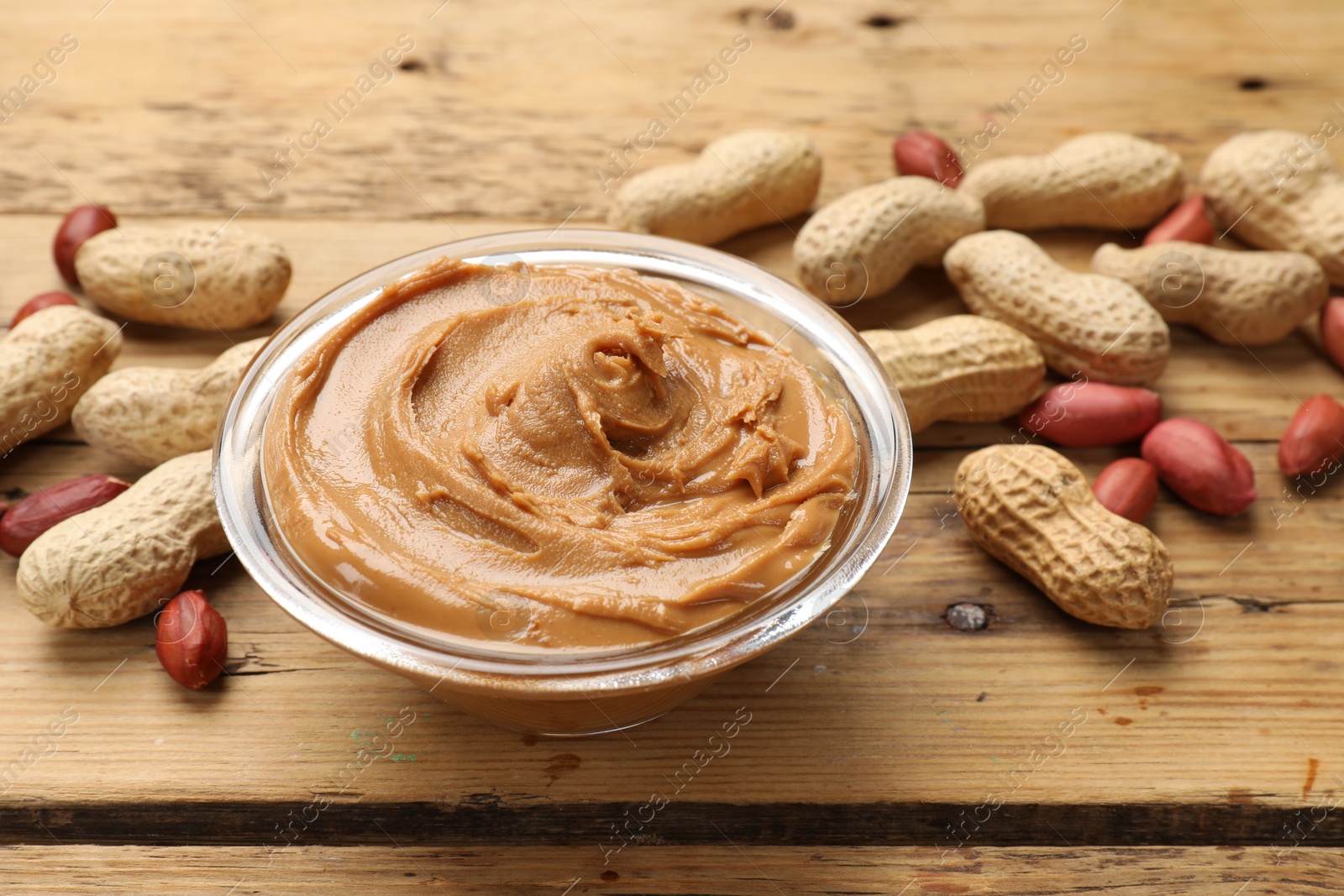 Photo of Tasty peanut butter in bowl and groundnuts on wooden table, closeup