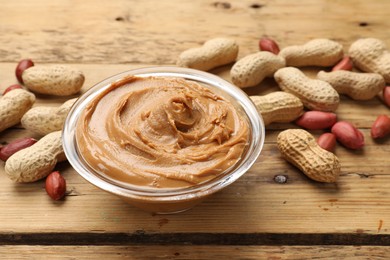 Tasty peanut butter in bowl and groundnuts on wooden table, closeup