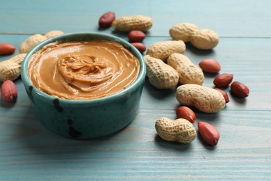 Tasty peanut butter in bowl and groundnuts on light blue wooden table, closeup