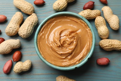 Photo of Tasty peanut butter in bowl and groundnuts on light blue wooden table, flat lay