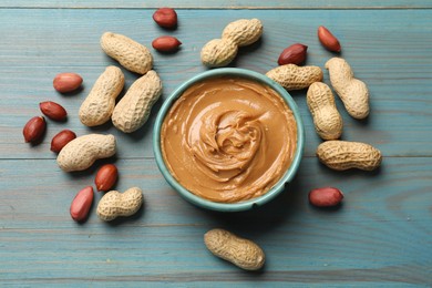 Photo of Tasty peanut butter in bowl and groundnuts on light blue wooden table, flat lay