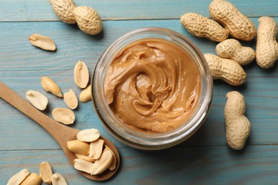 Tasty peanut butter in jar and groundnuts on blue wooden table, flat lay