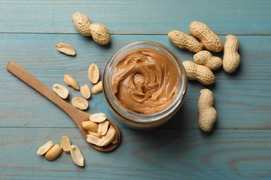 Tasty peanut butter in jar and groundnuts on blue wooden table, flat lay