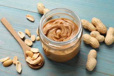 Tasty peanut butter in jar and groundnuts on blue wooden table