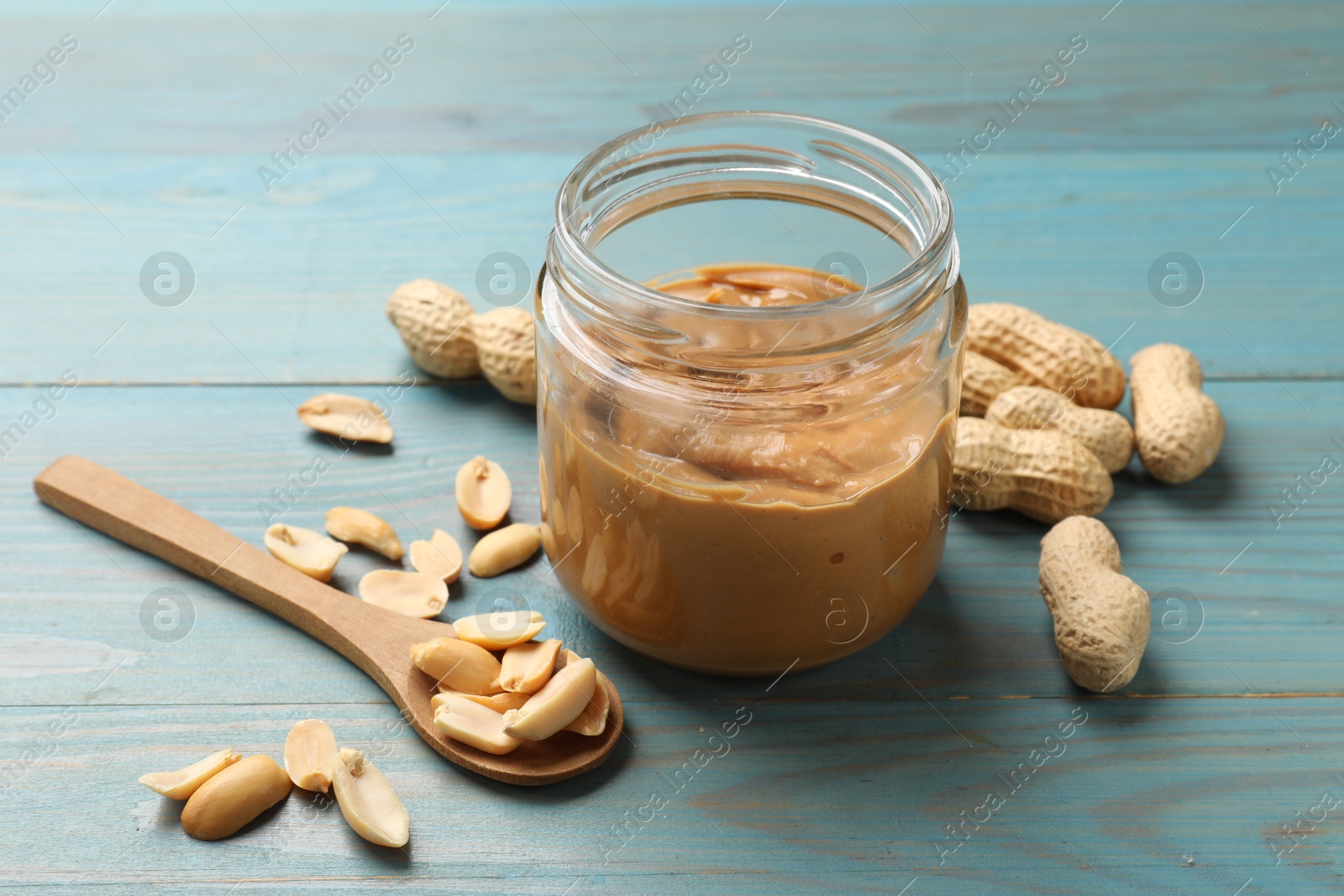 Photo of Tasty peanut butter in jar and groundnuts on blue wooden table