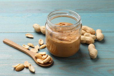 Tasty peanut butter in jar and groundnuts on blue wooden table