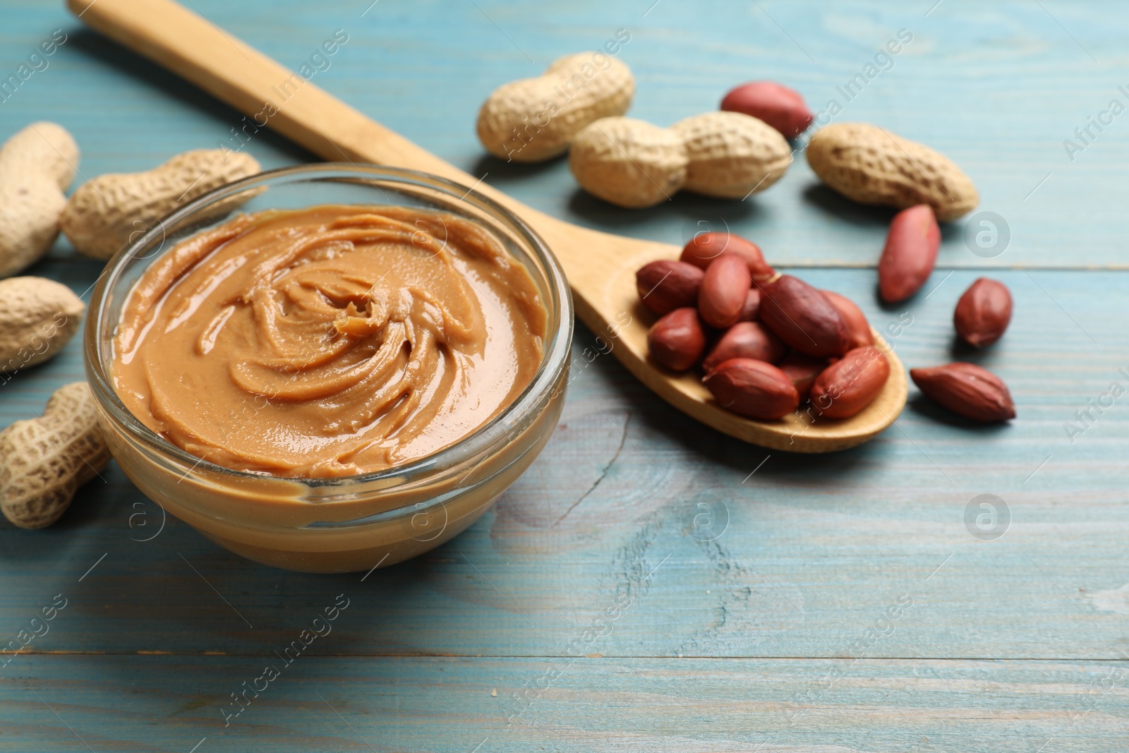 Photo of Tasty peanut butter in bowl and groundnuts on blue wooden table