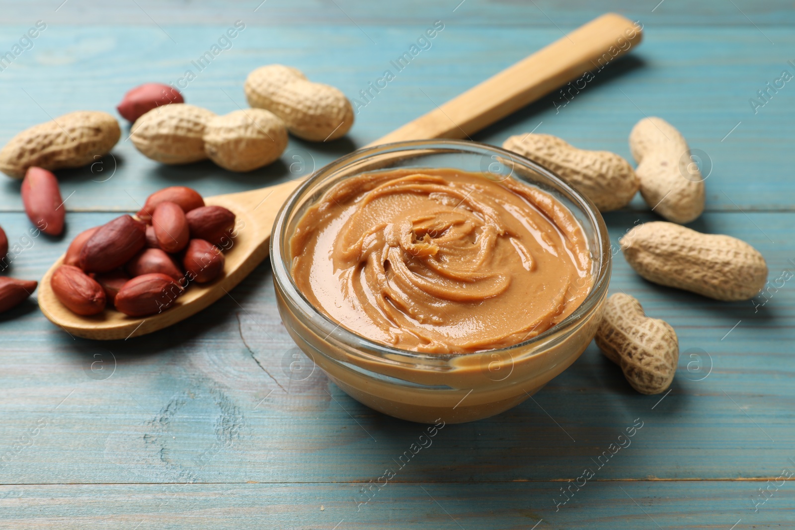 Photo of Tasty peanut butter in bowl and groundnuts on blue wooden table