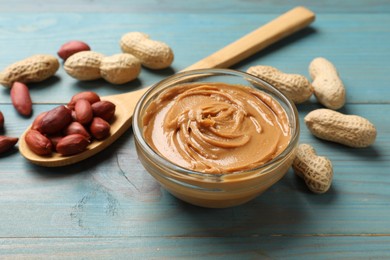 Tasty peanut butter in bowl and groundnuts on blue wooden table