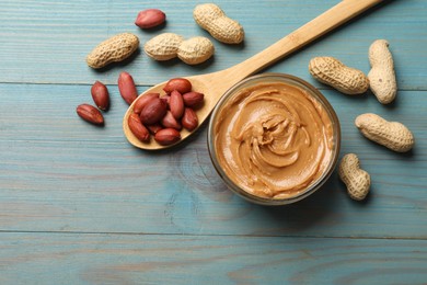 Photo of Tasty peanut butter in bowl and groundnuts on blue wooden table, flat lay