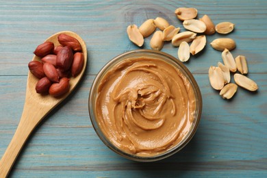 Tasty peanut butter in bowl and groundnuts on blue wooden table, flat lay