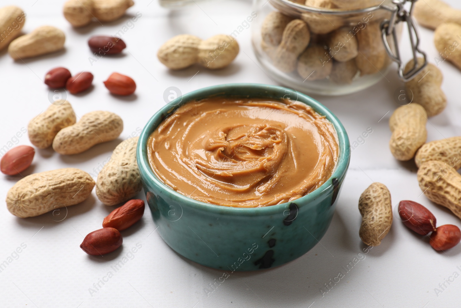 Photo of Tasty peanut butter in bowl and groundnuts on white table