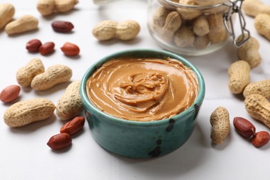 Photo of Tasty peanut butter in bowl and groundnuts on white table