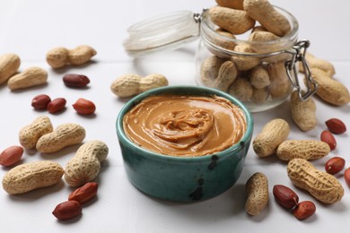 Photo of Tasty peanut butter in bowl and groundnuts on white table