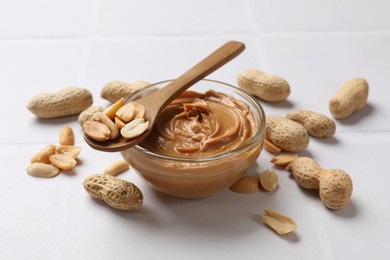 Tasty peanut butter in bowl and groundnuts on white tiled table