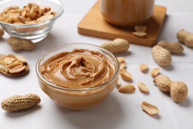 Tasty peanut butter in bowl and groundnuts on white tiled table