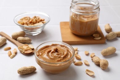 Tasty peanut butter in bowl and groundnuts on white tiled table