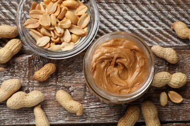 Tasty peanut butter in jar and groundnuts on wooden table, flat lay