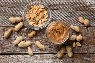 Photo of Tasty peanut butter in jar and groundnuts on wooden table, flat lay