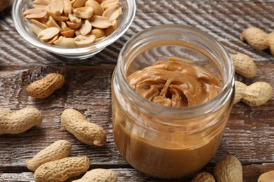 Tasty peanut butter in jar and groundnuts on wooden table