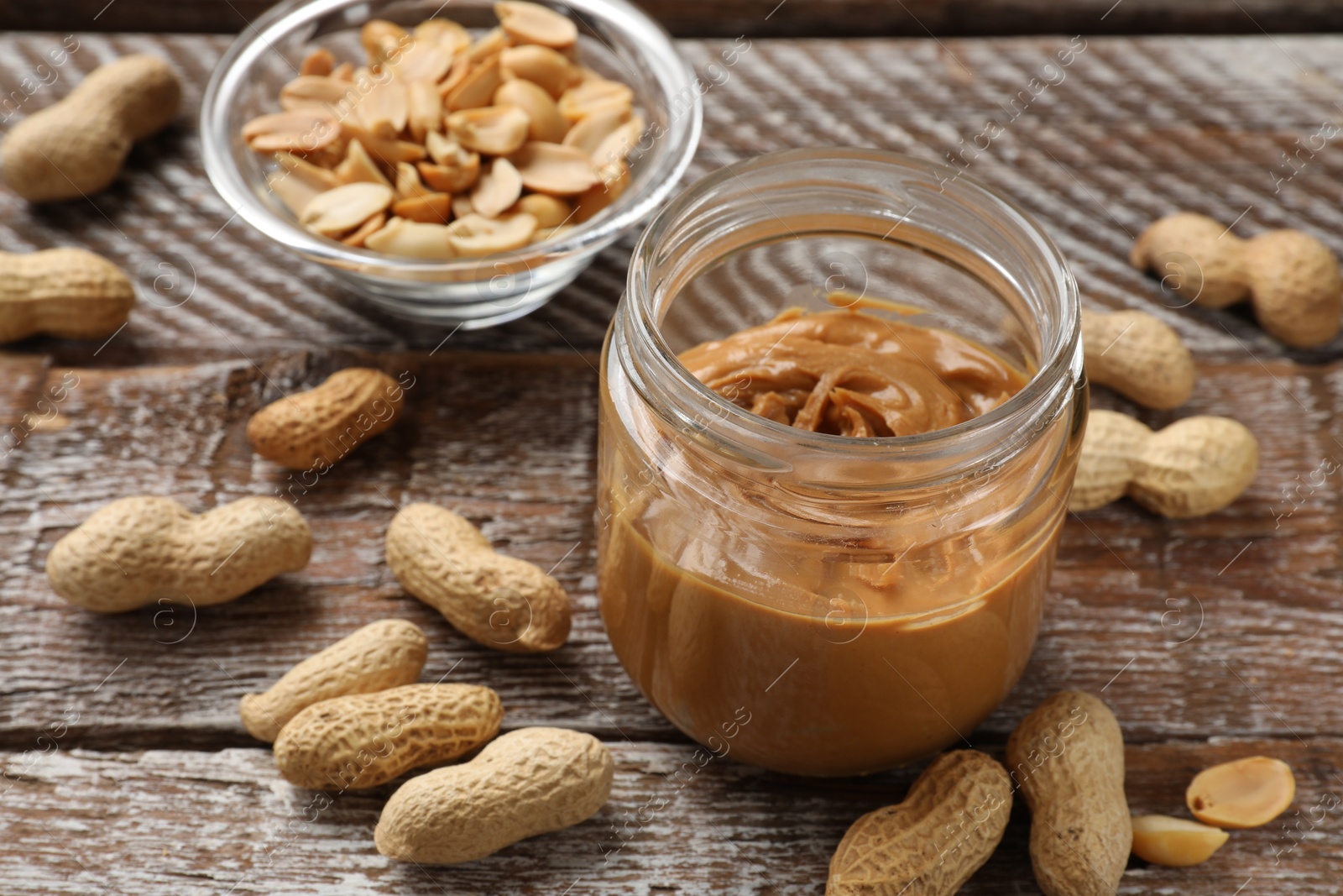 Photo of Tasty peanut butter in jar and groundnuts on wooden table