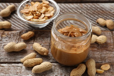 Tasty peanut butter in jar and groundnuts on wooden table