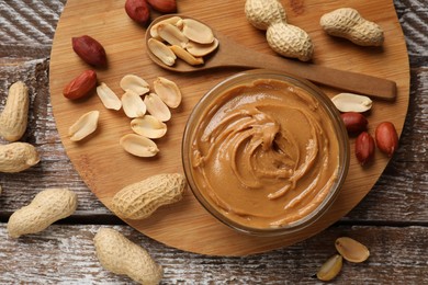 Photo of Tasty peanut butter in bowl and groundnuts on wooden table, flat lay