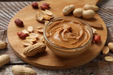 Photo of Tasty peanut butter in bowl and groundnuts on wooden table