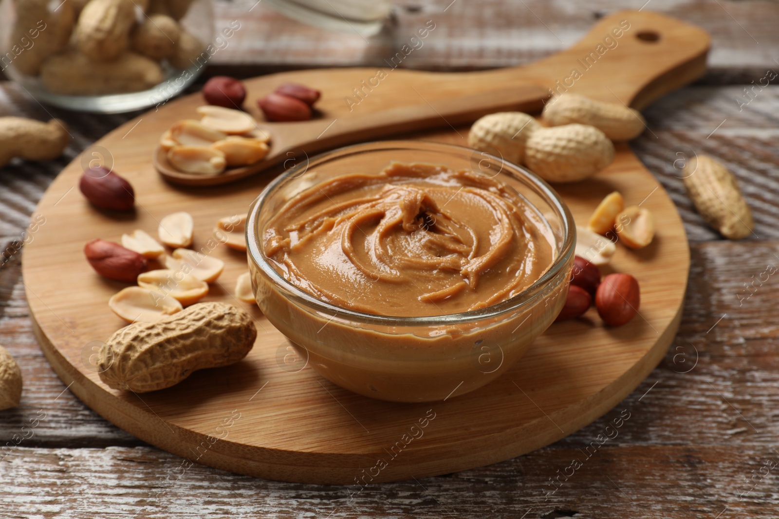 Photo of Tasty peanut butter in bowl and groundnuts on wooden table